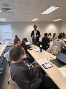 Instructor Michael DeBlois of YCCC stands before a class gesturing, with several rows of students seen from behind.