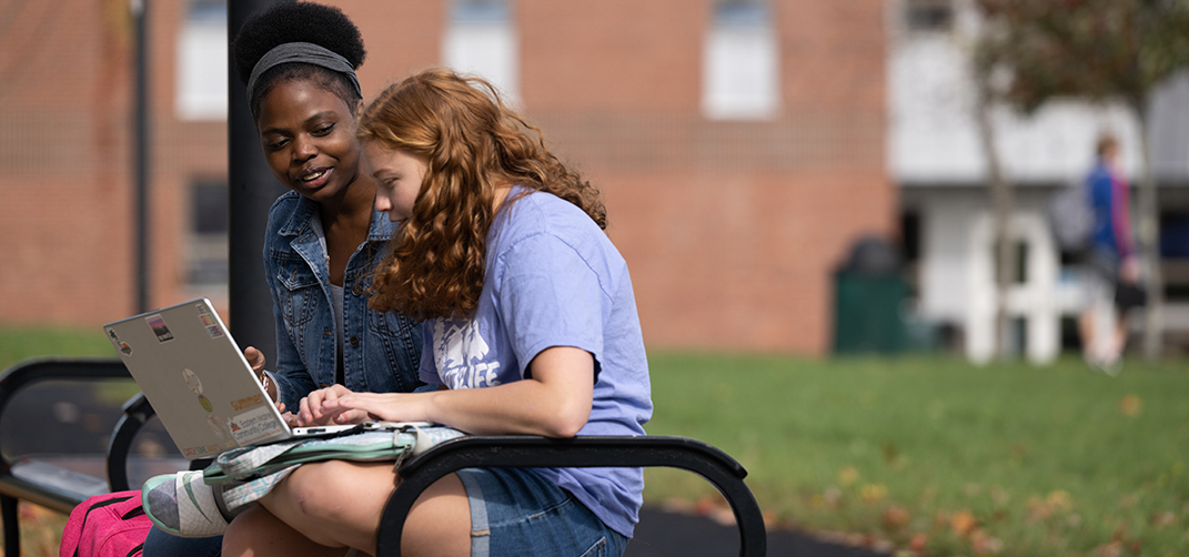 Two students sitting on a bench outside.