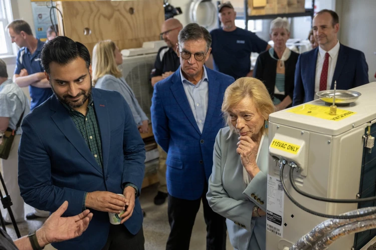 Governor Mills and other officials gather around a heat pump and listen to an instructor at the training lab at Kennebec Valley Community College.