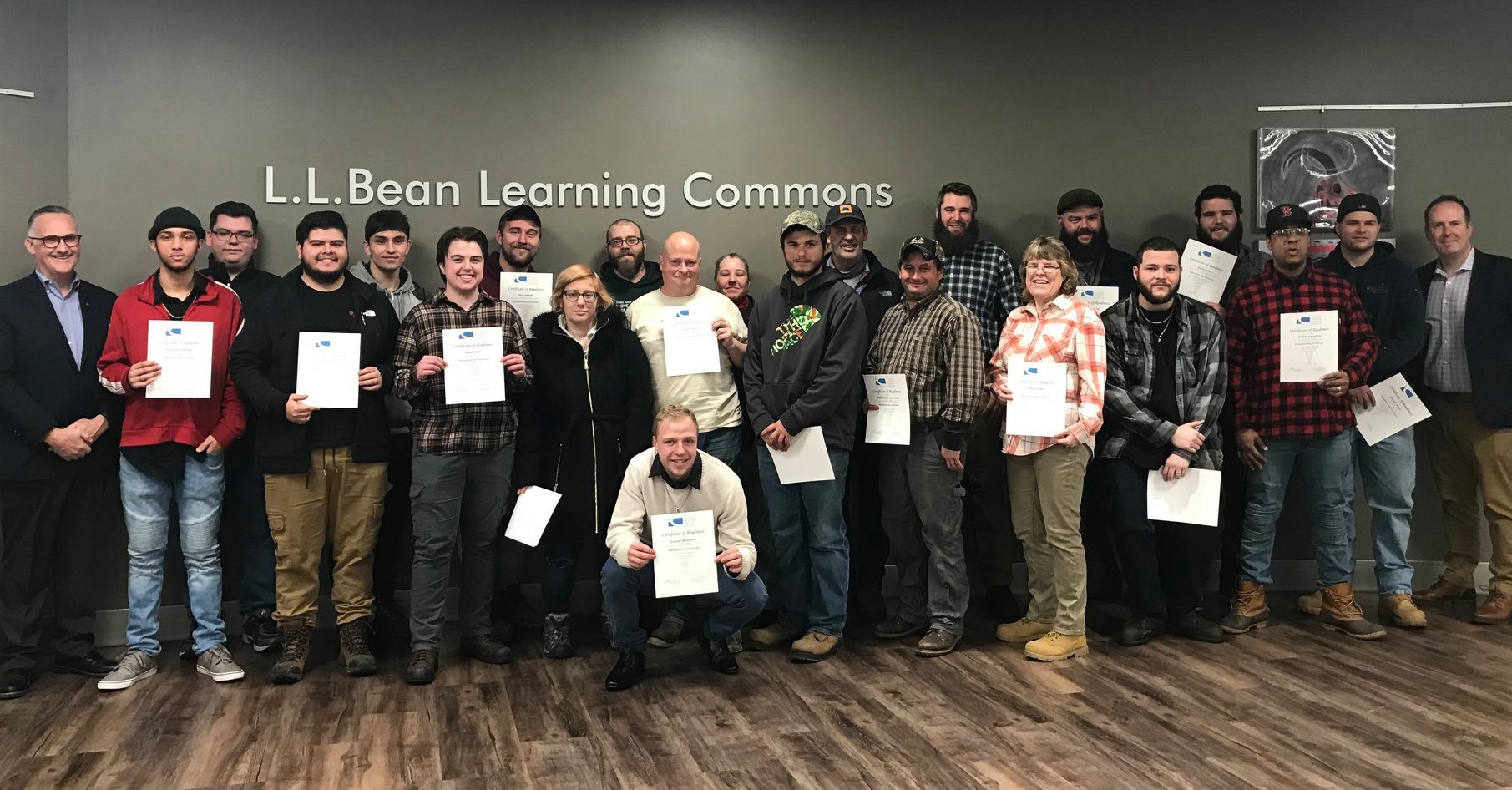 Group of about 20 men and women facing camera and holding up certificates.